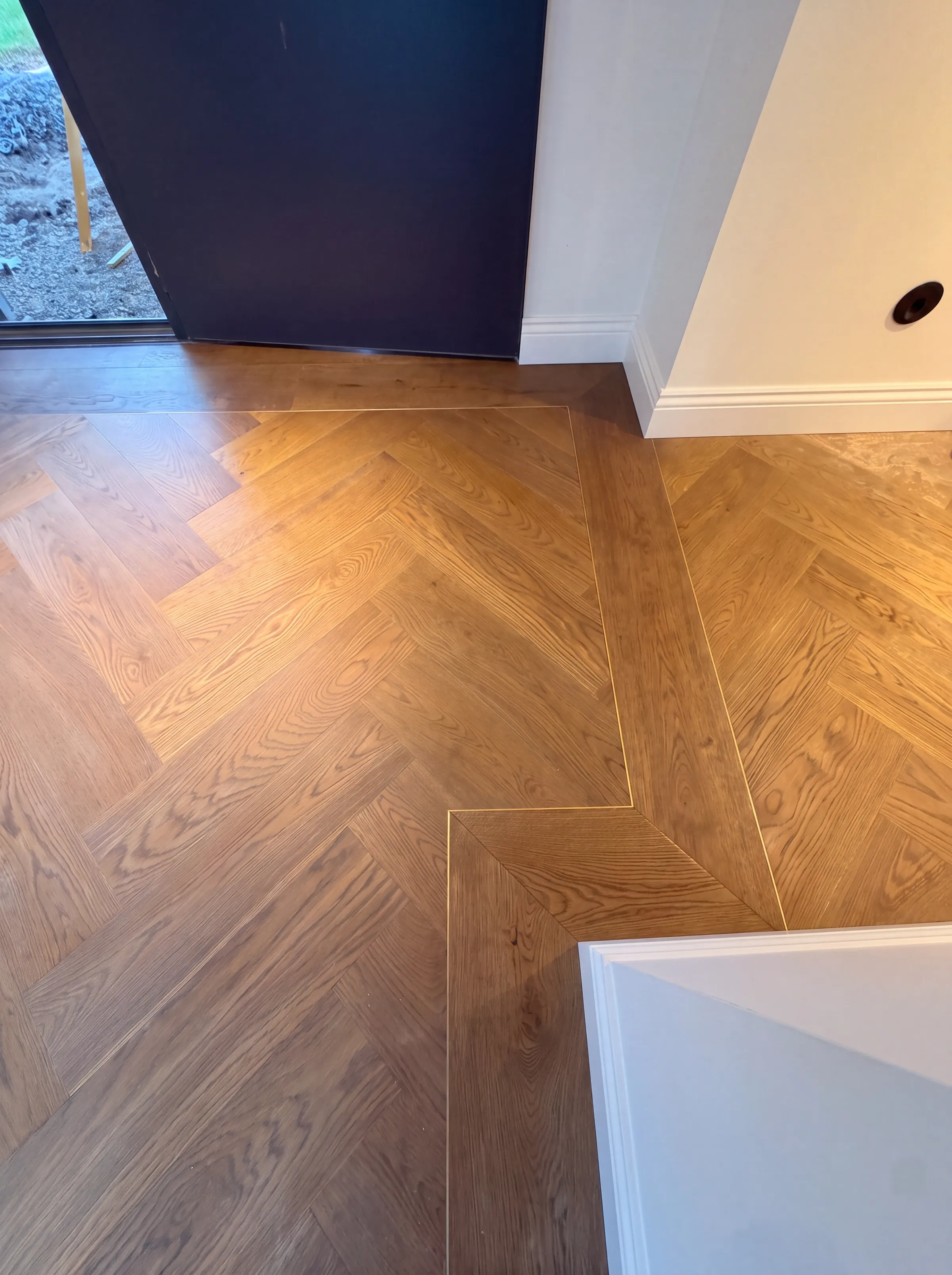 A herringbone field meeting its straight plank border with a slim brass channel between them, the ATS signature style