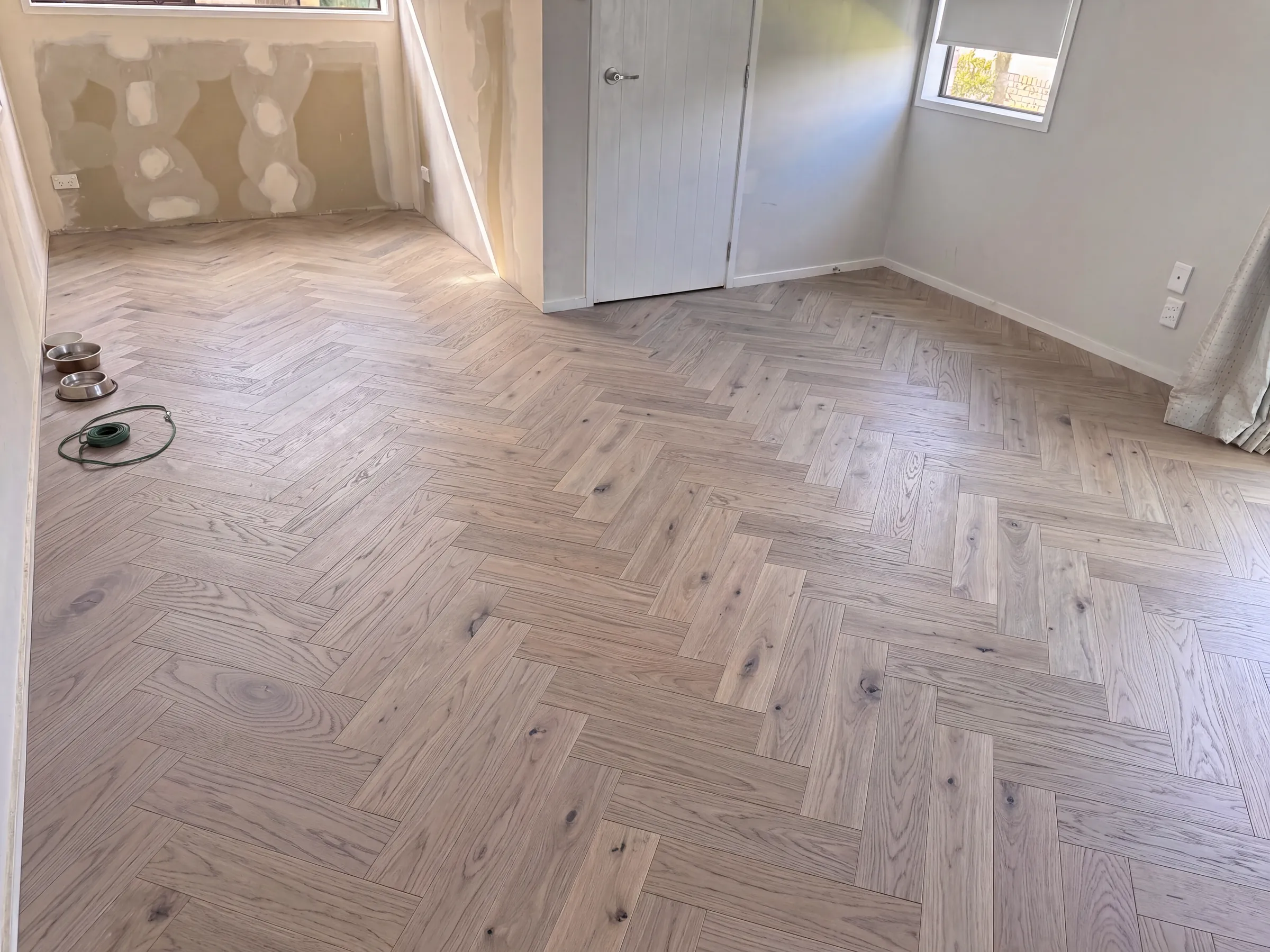 Ash herringbone engineered timber through a living room, the dog&rsquo;s bowls already down
