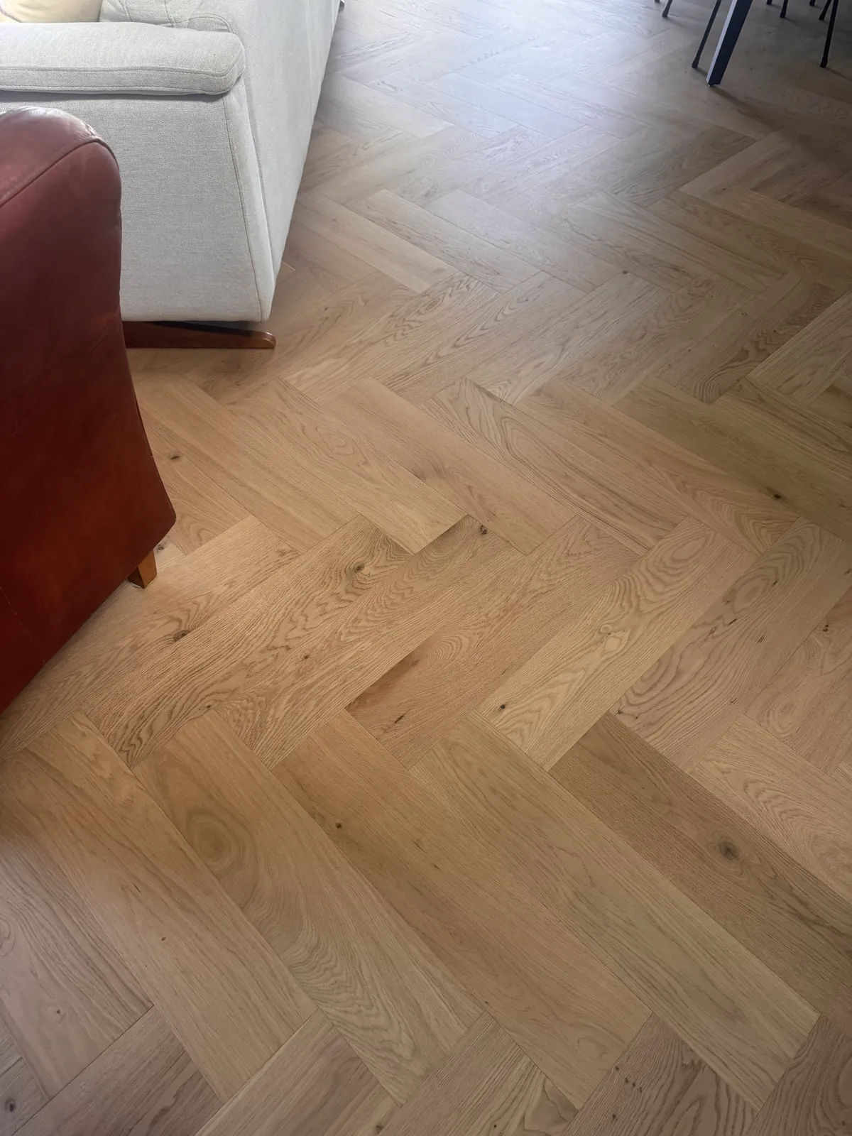 Natural Clear herringbone engineered timber up close beside the club chair at Whangaparaoa Road, Red Beach