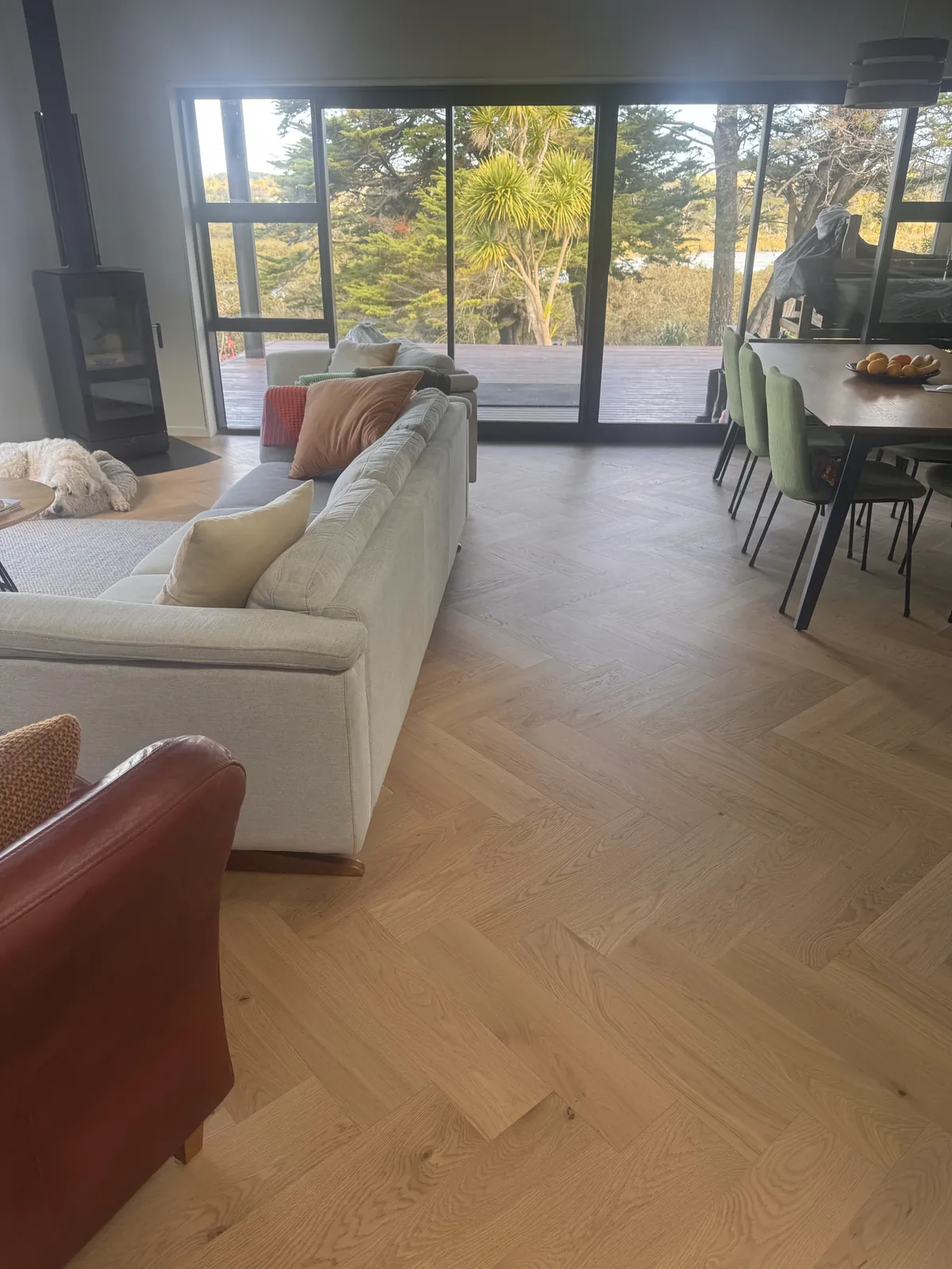 Natural Clear herringbone engineered timber in the furnished living room at Whangaparaoa Road, the dog asleep by the fire