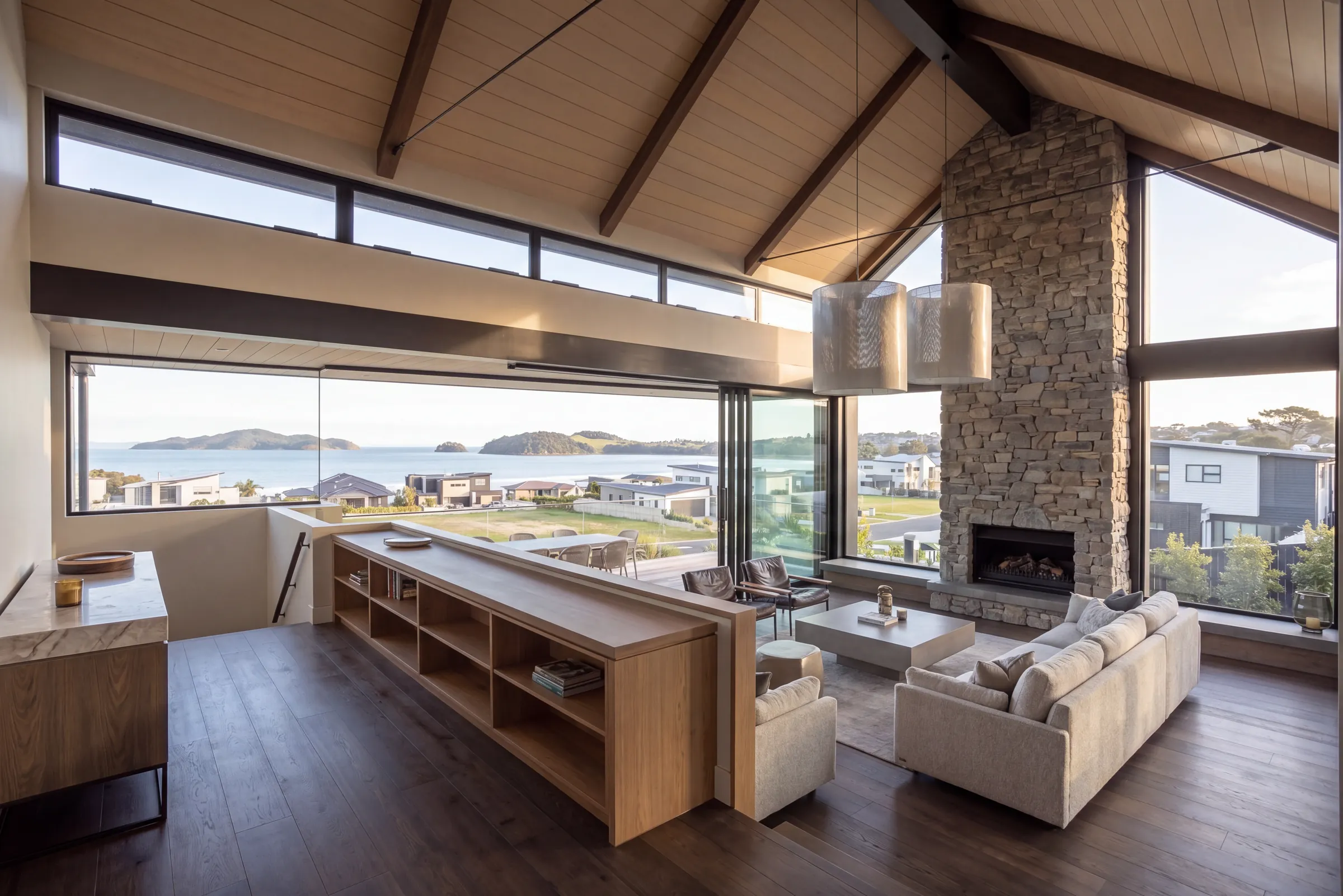 Nuage oak plank in a living room with a raked timber ceiling, stone fireplace and coastal view