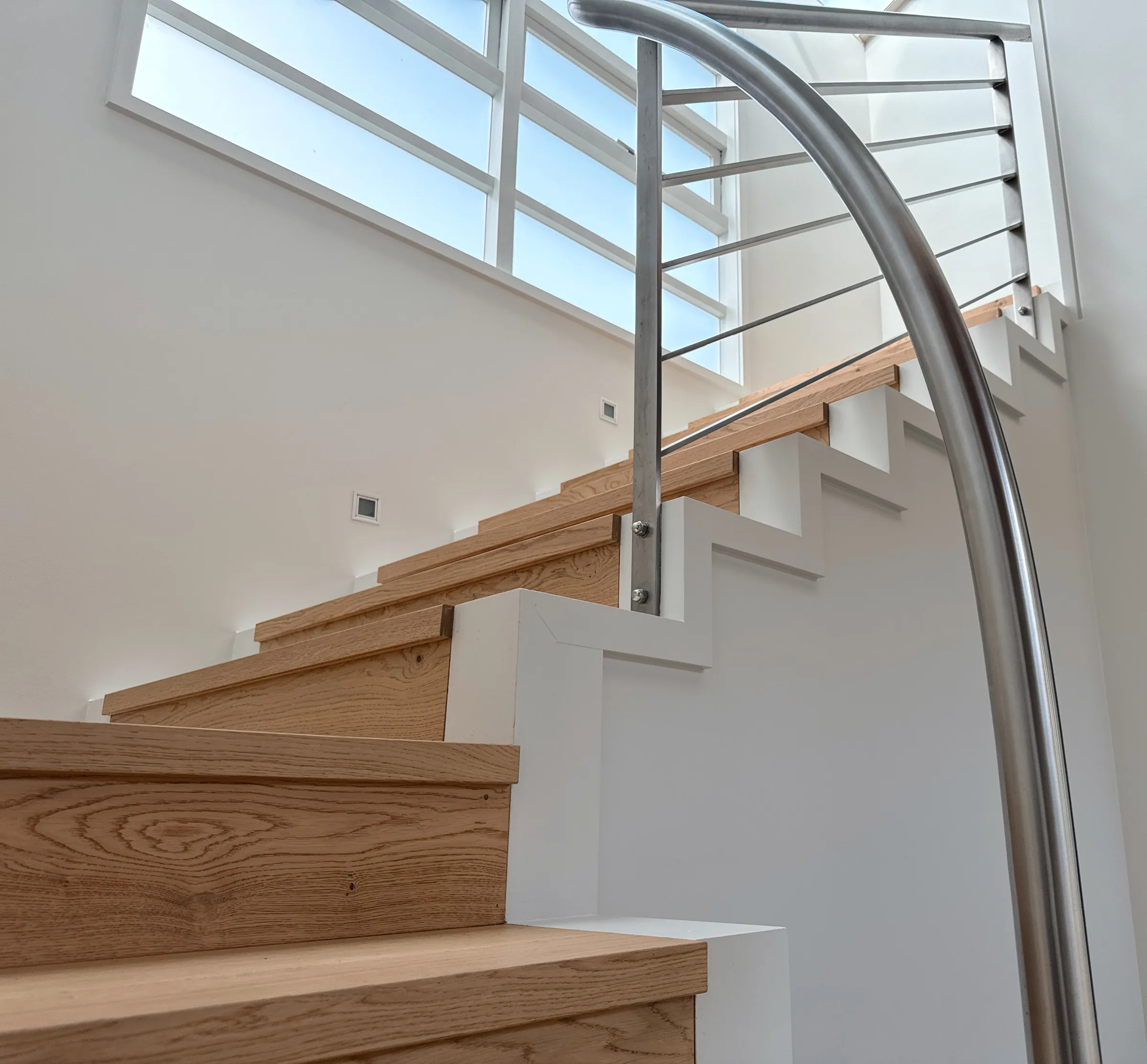 Stairs in the Oak Plank colour Western, with white risers and a curved steel handrail beneath a skylight, at Seacliffe Avenue, Belmont